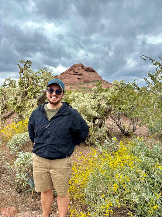 A man (me) standing in the desert botanical garden with yellow flowers around me and a big rock in the background.